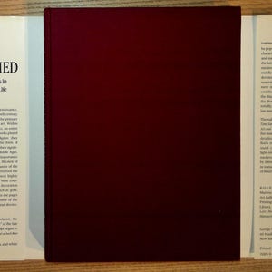 Puede incluir: Un libro de tapa dura titulado "Time Sanctified: The Book of Hours in Medieval Art and Life" de Roger S. Wieck. El libro tiene una cubierta de color burdeos oscuro y p&aacute;ginas blancas con texto. El libro est&aacute; abierto, revelando el t&iacute;tulo y el autor.