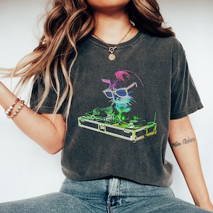 Op de afbeelding: Donkergrijs t-shirt met een kleurrijke afbeelding van een kat met een zonnebril die draait op een draaitafel. De kat is afgebeeld in levendige neonkleuren, wat zorgt voor een leuk en opvallend ontwerp. Het t-shirt heeft een vintage, gewassen look.
