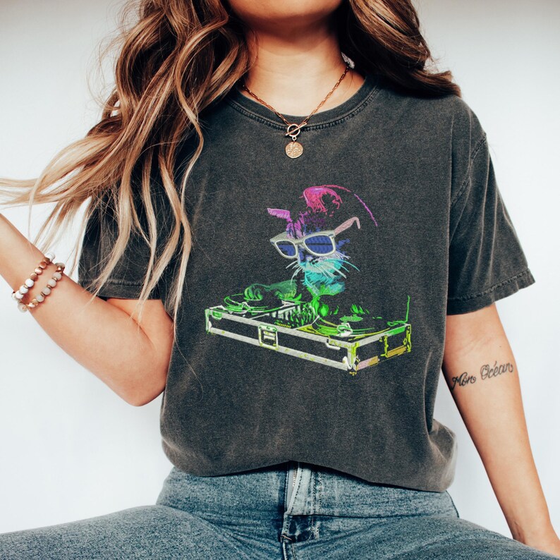 Op de afbeelding: Donkergrijs t-shirt met een kleurrijke afbeelding van een kat met een zonnebril die draait op een draaitafel. De kat is afgebeeld in levendige neonkleuren, wat zorgt voor een leuk en opvallend ontwerp. Het t-shirt heeft een vintage, gewassen look.