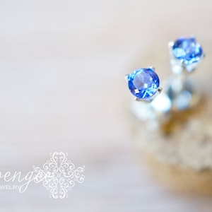 May include: A pair of silver stud earrings with small, round, blue gemstones.