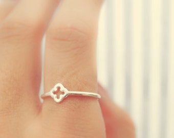 May include: A silver ring with a delicate, openwork design in the shape of a four-leaf clover. The ring is worn on a finger.