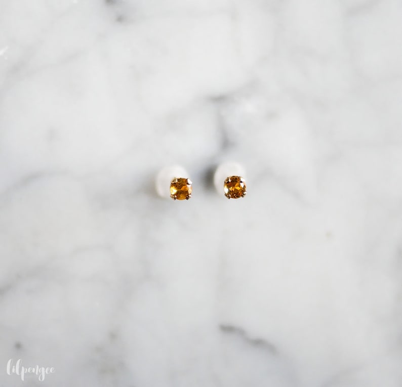 May include: A pair of gold stud earrings with small, square-shaped, orange gemstones.