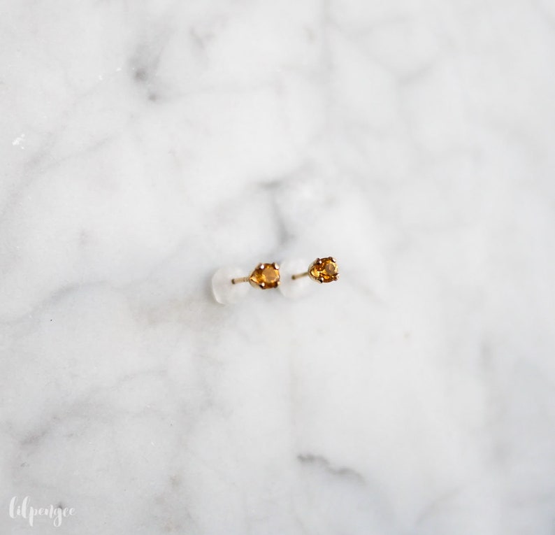 May include: A pair of gold stud earrings with small, oval-shaped, orange gemstones.