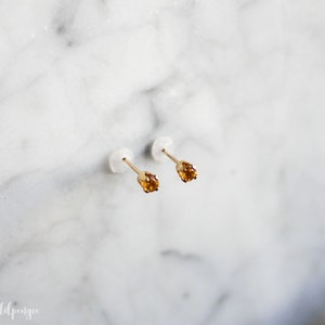 May include: A pair of gold stud earrings with small, round, orange gemstones.