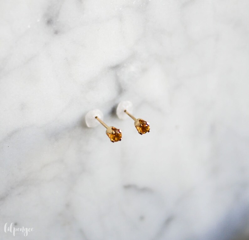 May include: A pair of gold stud earrings with small, round, orange gemstones.