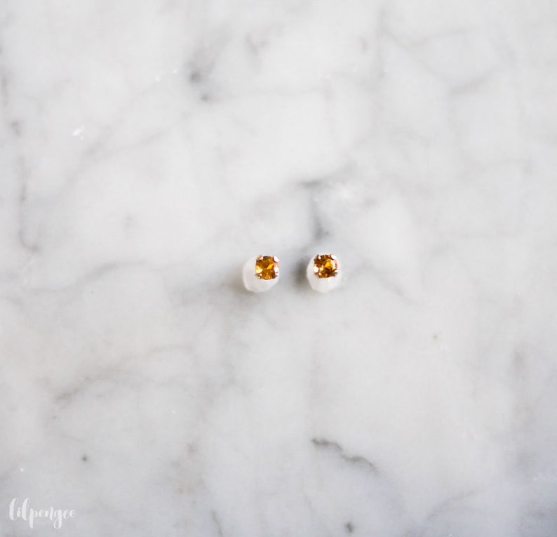 May include: A pair of small, silver stud earrings with a square, orange gemstone in the center of each.