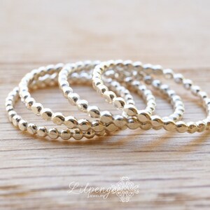 May include: Four silver beaded stacking rings. The rings are made of small, round beads that are connected together to form a continuous circle. The rings are stacked on top of each other, with the largest ring at the bottom and the smallest ring at the top.
