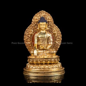 May include: A gold Buddha statue, seated with detailed robes and a halo. The statue has a calm expression and is set against a black backdrop. The base is also decorated with detailed carvings, reflecting a sense of peace.