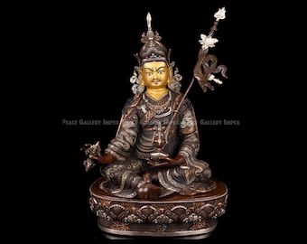 May include: A detailed bronze statue of a seated figure with a gold face, ornate headdress, and elaborate clothing. The statue holds objects in its hands and is set on a decorative base with turquoise accents. The background is black.