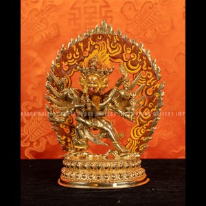 May include: A gold-coloured statue of a multi-armed deity with multiple faces, set against an orange backdrop. The statue has intricate details, including a halo and ornate base. The overall theme is religious or spiritual.
