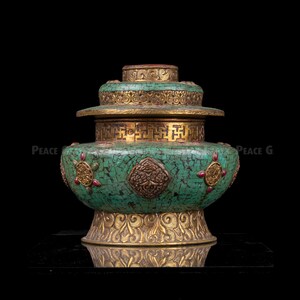 May include: An ornate, antique-style vessel with a turquoise mosaic exterior and gold-colored accents. The vessel features intricate patterns and designs, including a decorative lid and base. The overall aesthetic is reminiscent of traditional craftsmanship.