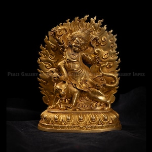 May include: A golden statue of a deity with a fierce expression, surrounded by flames. The deity is depicted riding a tiger. The statue has intricate details and is set against a black background. The statue is a religious or spiritual item.