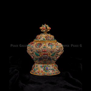 Puede incluir: Un jarrón decorativo dorado y ornamentado con tapa, adornado con piedras preciosas de colores. El jarrón presenta intrincados patrones y diseños, con piedras rojas, verdes y azules. La base y la tapa también están adornadas con detalles similares. El texto "Peace Gallery" es visible.