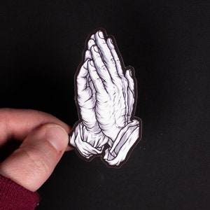 May include: A black and white sticker of two hands clasped in prayer.