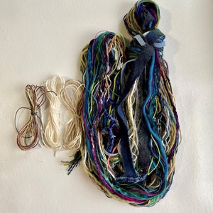 May include: A collection of colorful yarn and string, including a bundle of multi-colored yarn, two skeins of white yarn, and a small bundle of brown yarn.