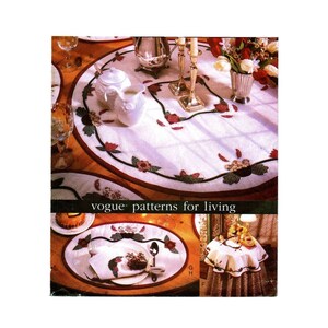 May include: A set of three quilted table linens featuring a floral design in shades of red, green, and white. The linens include a large oval table runner, a smaller oval placemat, and a round table runner. The linens are made by Vogue Patterns for Living.