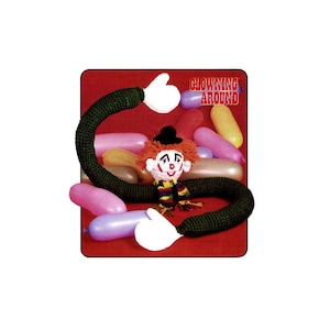 May include: A green crocheted clown with a red and white face and a black hat. The clown is surrounded by colorful balloons. The text "CLOWNING AROUND" is in red letters on a white background.