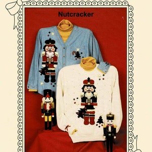 May include: A craft pattern for a Nutcracker sweater. The pattern features a blue denim sweater with a Nutcracker design and a white sweater with a Nutcracker design. The pattern is from Ozark Crafts and includes instructions for making the sweaters.