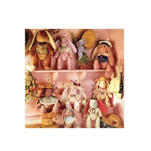 May include: A collection of eight handmade fabric bunny rabbits, each with unique clothing and accessories. The bunnies are displayed on a shelf with a pink background.