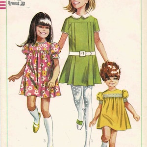 May include: A vintage Simplicity sewing pattern for girls' dresses. The pattern number is 7565 and the price is 60 cents. The pattern includes three different dress styles: a green dress with a white collar, a pink floral dress, and a yellow dress with a white lace trim.