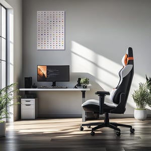 May include: A white desk with a black computer monitor, a keyboard, and a black and orange gaming chair. The desk is against a white wall with a framed print of a grid of colorful icons.