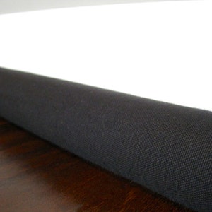 May include: A black fabric doorstop, rolled up and placed against a white baseboard and a dark wood floor.
