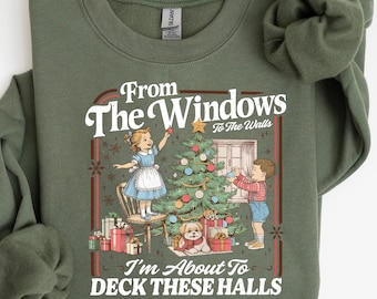 May include: Olive green sweatshirt with a festive graphic. The graphic features a vintage illustration of children decorating a Christmas tree, with the text "From The Windows To The Walls, I'm About To Deck These Halls."