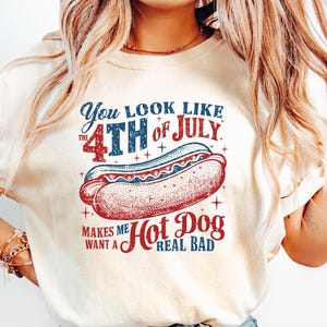 Op de afbeelding: Cr&egrave;mekleurig T-shirt met een afbeelding van een hotdog en de tekst "You look like the 4th of July makes me want a hot dog real bad." Het ontwerp bevat rood, wit en blauw.
