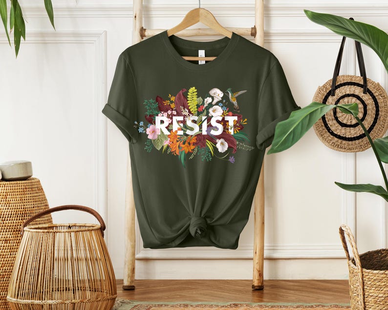 May include: A green t-shirt with a floral design and the word "RESIST" in white letters.