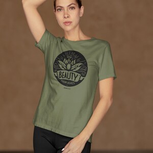 Könnte beinhalten: Ein grünes T-Shirt mit einem schwarzen Kreis-Motiv, das eine Blume und den Text "Beauty from Ashes" mit dem Bibelvers "Isaiah 43:19" zeigt.