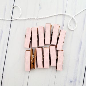 May include: A set of 10 wooden clothespins with a pink polka dot pattern. The clothespins are arranged in a rectangular shape.