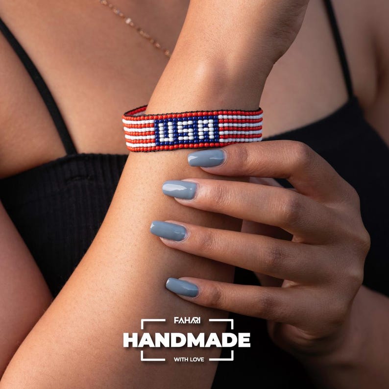 May include: A red, white, and blue beaded bracelet with the word "USA" in the center. The bracelet is handmade and has a "FAHARI HANDMADE WITH LOVE" label.