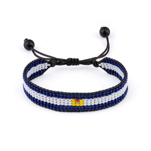 May include: Adjustable beaded bracelet featuring a pattern of blue, white, and black beads. The bracelet has a small, colorful accent and black adjustable cords with black ball ends. A stylish accessory for everyday wear.