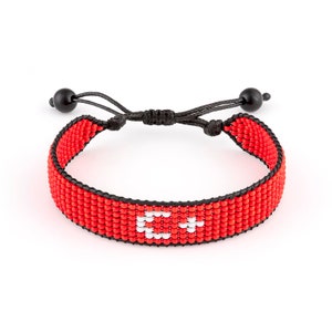 Puede incluir: Pulsera roja de cuentas con un dije blanco en forma de "C". La pulsera es ajustable con cordón negro y cuentas negras en los extremos.