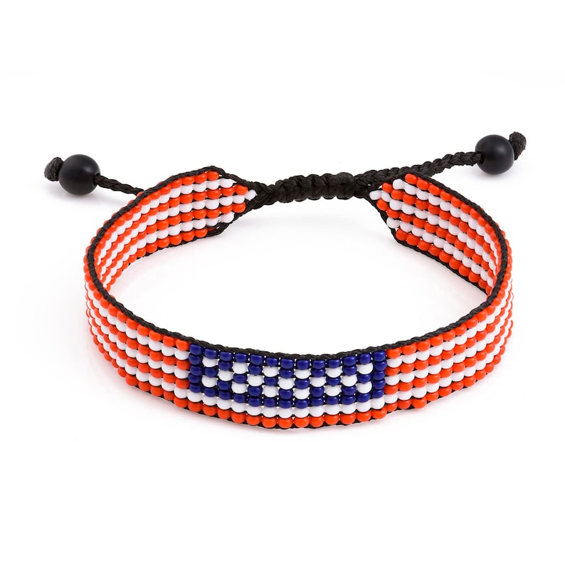 May include: A red, white, and blue beaded bracelet with a flag design. The bracelet is adjustable with a black cord and black beads at the ends.
