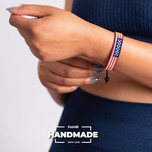 May include: A red, white, and blue beaded bracelet with an American flag design. The bracelet is adjustable with a black cord and bead. The bracelet is handmade with love.