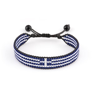 May include: A blue and white beaded bracelet with a black cord and adjustable closure. The beads are arranged in a pattern that resembles the Greek flag.