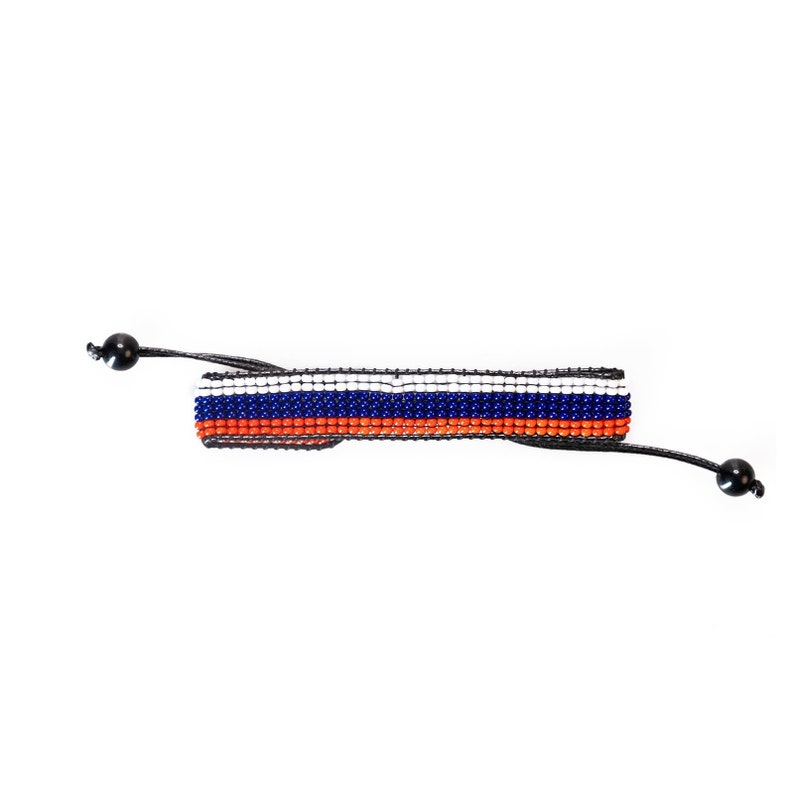 Op de afbeelding: Een zwarte kralen armband met een geweven ontwerp in oranje, wit en blauw.
