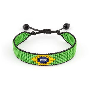May include: A woven beaded bracelet featuring a vibrant lime green background with a central eye-shaped motif composed of yellow, dark blue, and white beads. The bracelet is secured with a black cord featuring an adjustable sliding knot closure.