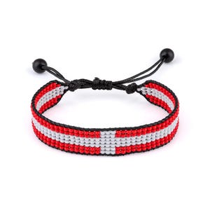 May include: A woven beaded bracelet featuring a horizontal pattern of red and white beads arranged in a cross design. The bracelet is secured with a black cord featuring an adjustable sliding knot mechanism and two small black spherical beads at the ends.