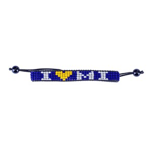 Puede incluir: Una pulsera de cuentas con el texto "I MI" en cuentas blancas sobre un fondo azul, con un símbolo de corazón amarillo. La pulsera tiene cordones negros ajustables y cuentas negras en cada extremo.
