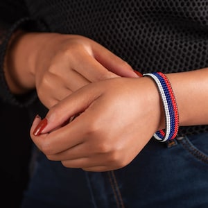 Op de afbeelding: Een kralen armband met rode, witte en blauwe strepen. De armband wordt om de pols gedragen.