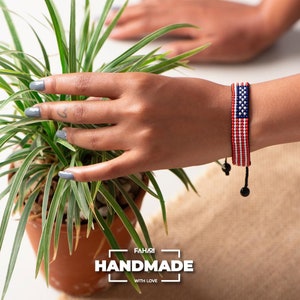 May include: A beaded bracelet with the American flag design. The bracelet is made with red, white, and blue beads and has a black cord with a black bead at the end. The bracelet is handmade and says "FAHARI HANDMADE WITH LOVE" on the bottom of the image.