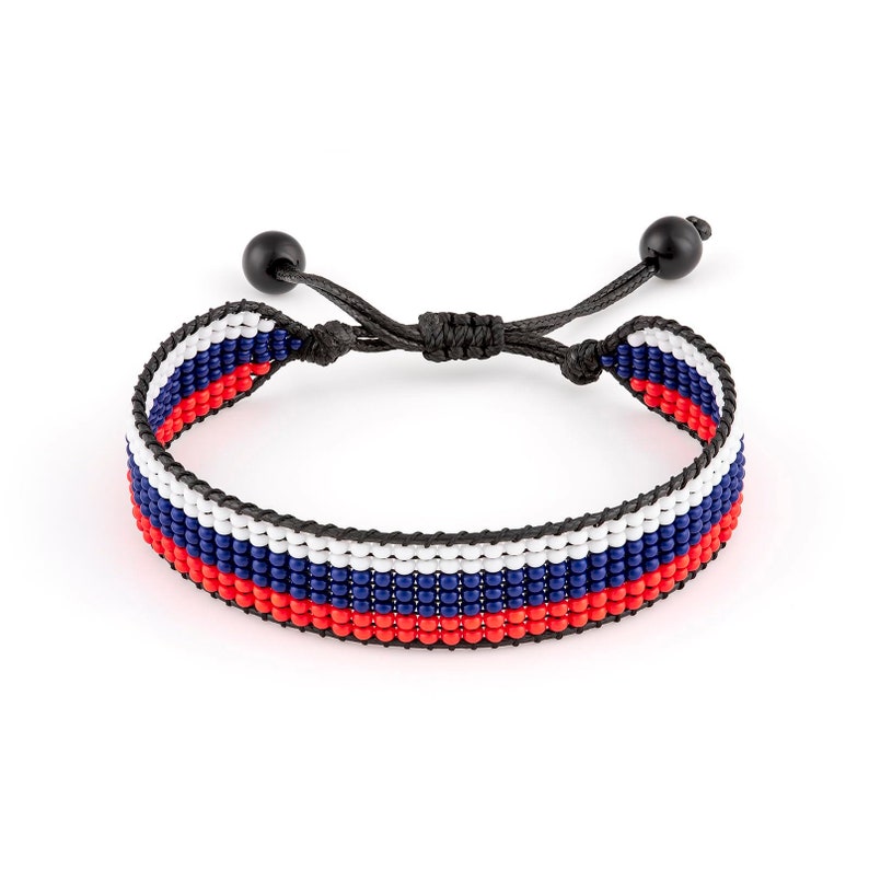 Op de afbeelding: Een zwarte kralen armband met rode, witte en blauwe strepen. De armband is verstelbaar met zwarte koordsluitingen.