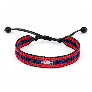 May include: Red, white, and blue beaded bracelet with a black cord and adjustable closure. The beads are arranged in a pattern that resembles a flag.