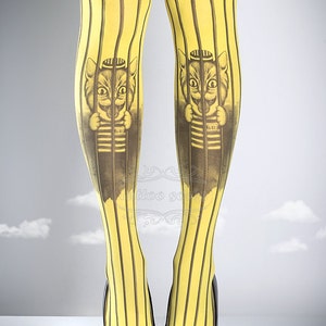 Puede incluir: Mallas amarillas con rayas negras y estampado gr&aacute;fico de un gato con una camisa a rayas y un sombrero, con el n&uacute;mero 6821 en la camisa, detr&aacute;s de las rejas.