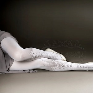 May include: White thigh-high stockings with lace-up detailing against a white background.