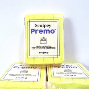 May include: Yellow Sculpey Premo oven-bake clay packages. Each package is 2 oz (57 g). The packaging has a white and blue label with the brand name, product name, and oven icon. The text on the label is in English, French, and Spanish.