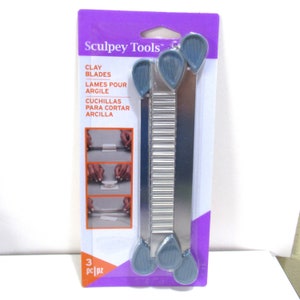 May include: A package of three Sculpey Tools clay blades. The blades are silver with blue handles. The package is purple and white with the text "Sculpey Tools", "Clay Blades", "Lames Pour Argile", "Cuchillas Para Cortar Arcilla", and "3 pc|pz".