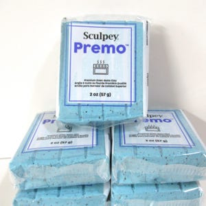 Puede incluir: Varios paquetes de arcilla polimérica Sculpey Premo. Cada paquete es de color azul claro y está envuelto en plástico transparente. La etiqueta dice "Sculpey Premo" y "2 oz (57 g)". La arcilla es para hornear de calidad superior.